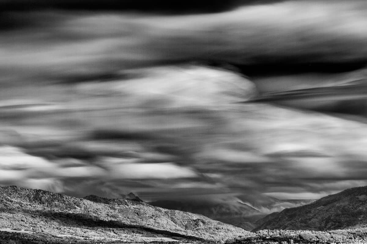 Infrared fine art black and white photograph of the Haute-Savoie mountains with clouds drifting above in a timeless landscape