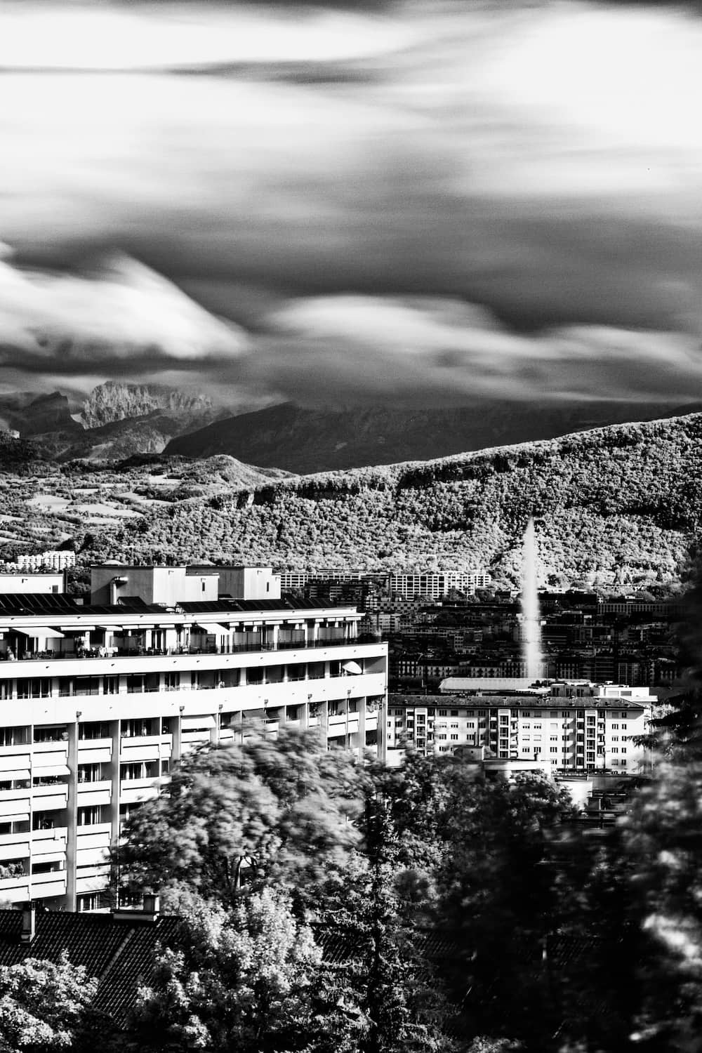 Infrared black and white fine art photograph of the Jet d'Eau in Geneva with mountains and clouds dancing together, taken from my balcony