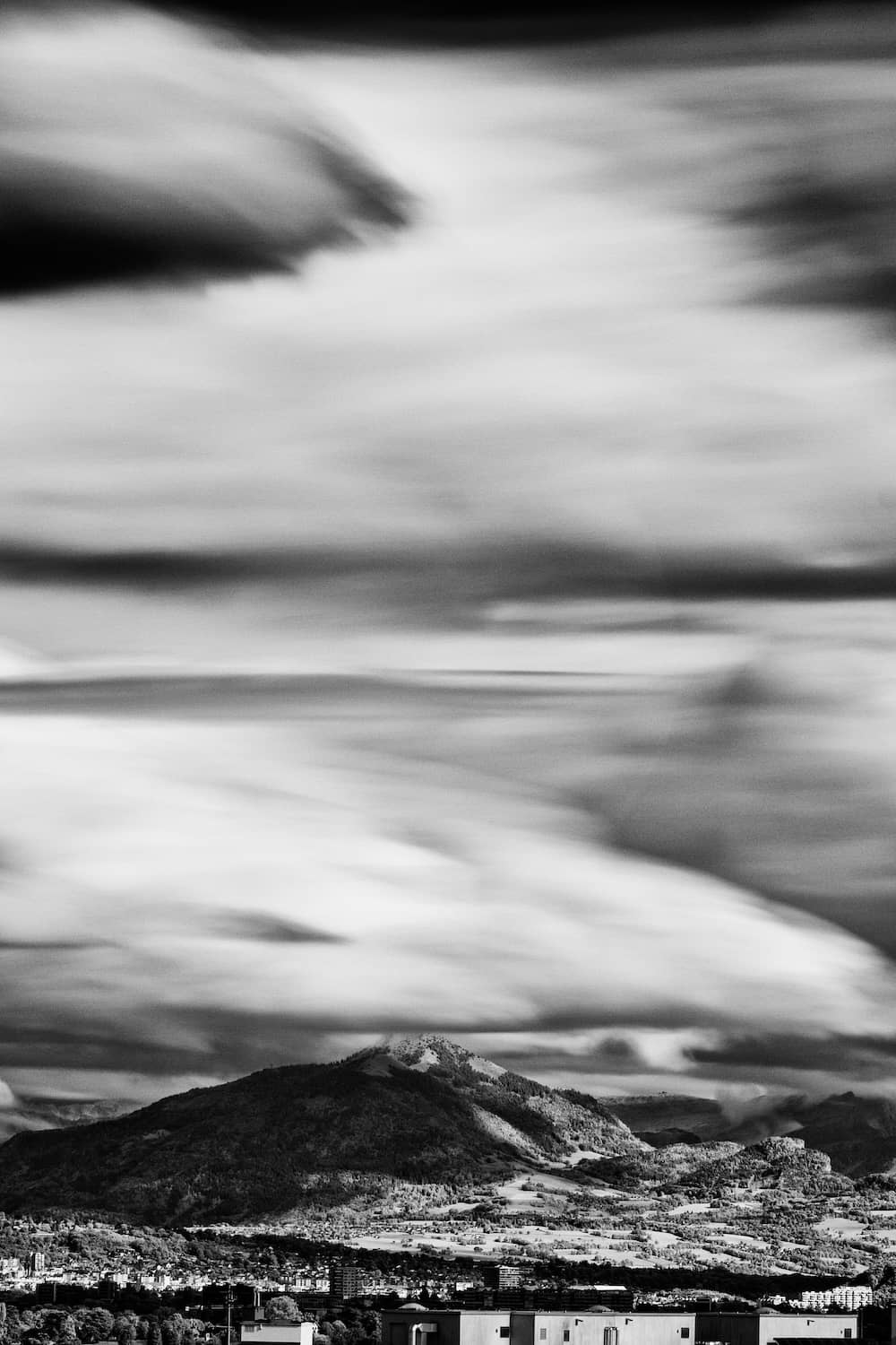 Infrared black and white fine art photograph of the Môle and Haute-Savoie mountains with clouds drifting above, taken in Geneva
