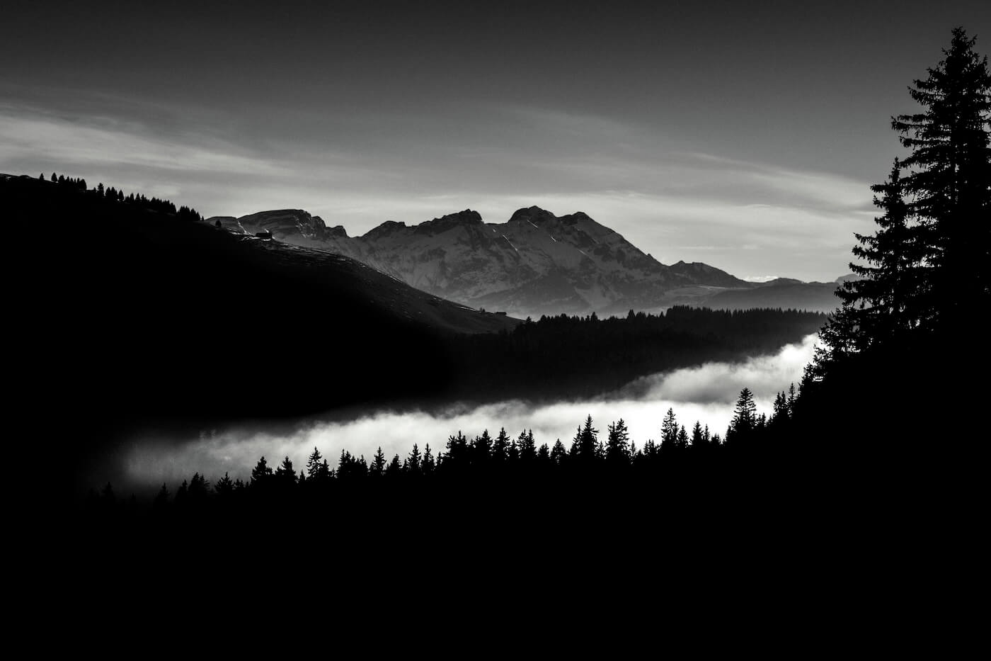 Black and white landscape of a sea of clouds flowing into a mountain valley, creating an ethereal atmosphere