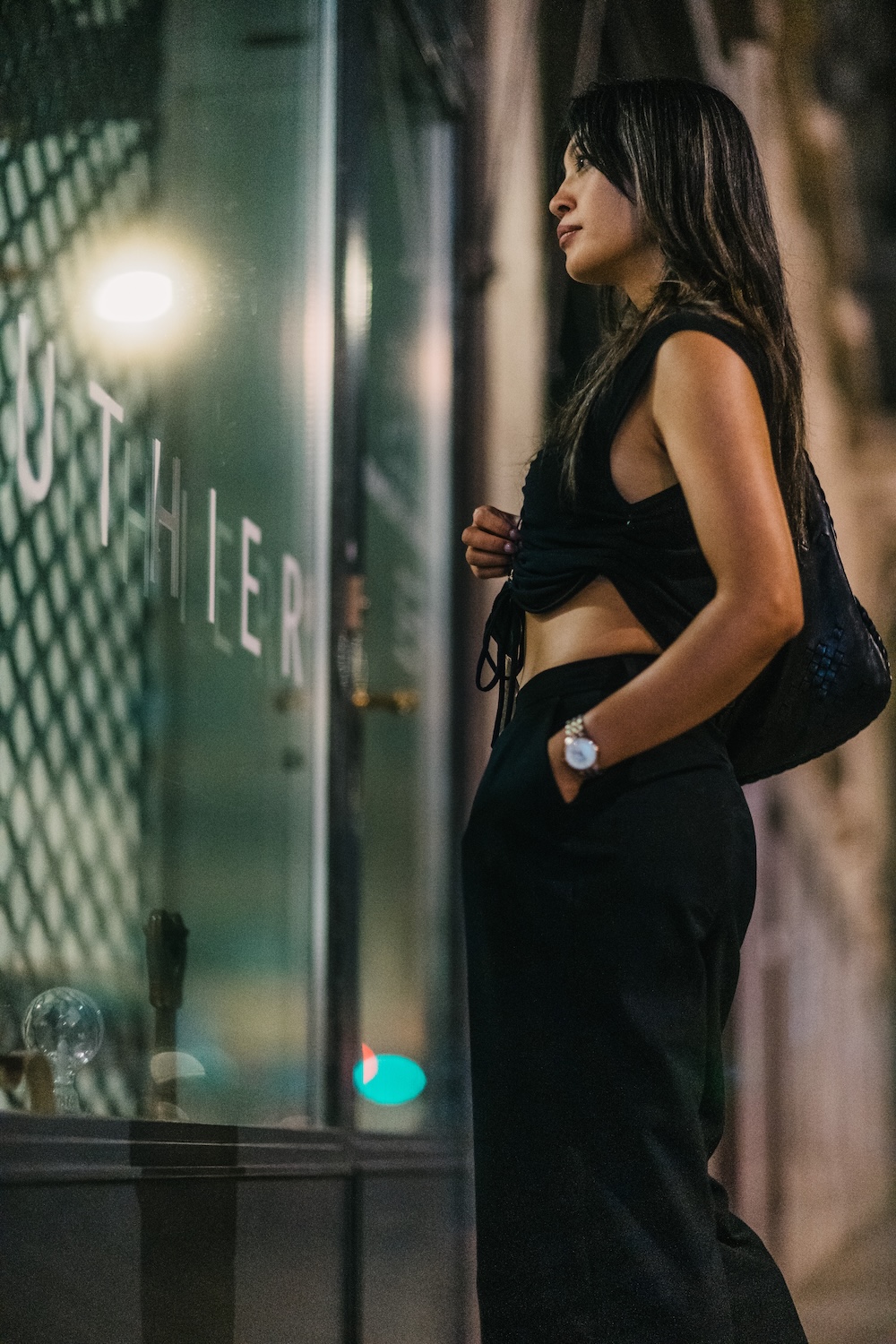 Cinematic lifestyle portrait of a woman looking at a shop window at night with her reflection clearly visible in the window, giving a cinematic and filmic touch to the image