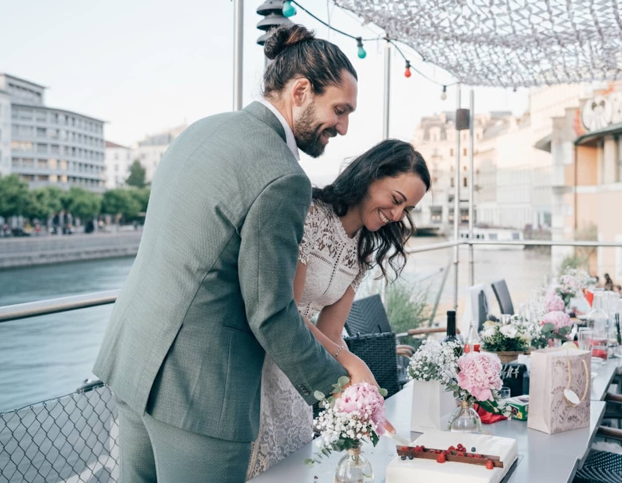 Candid cinematic shot of a bride and groom smiling while cutting their wedding cake at the Bateau-Lavoir overlooking the Rhône in Geneva.