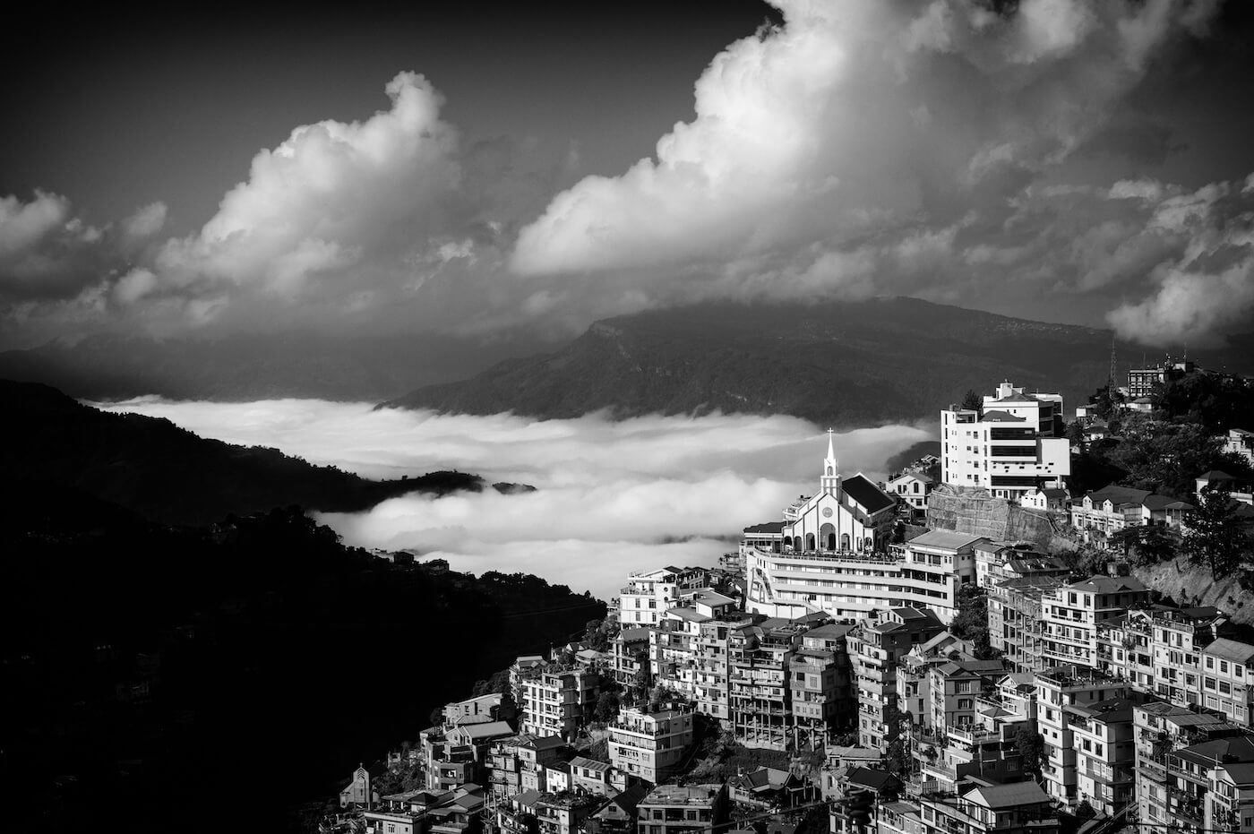 Fine art black and white photograph of Aizawl, India, with the city bathed in drifting clouds over the hills