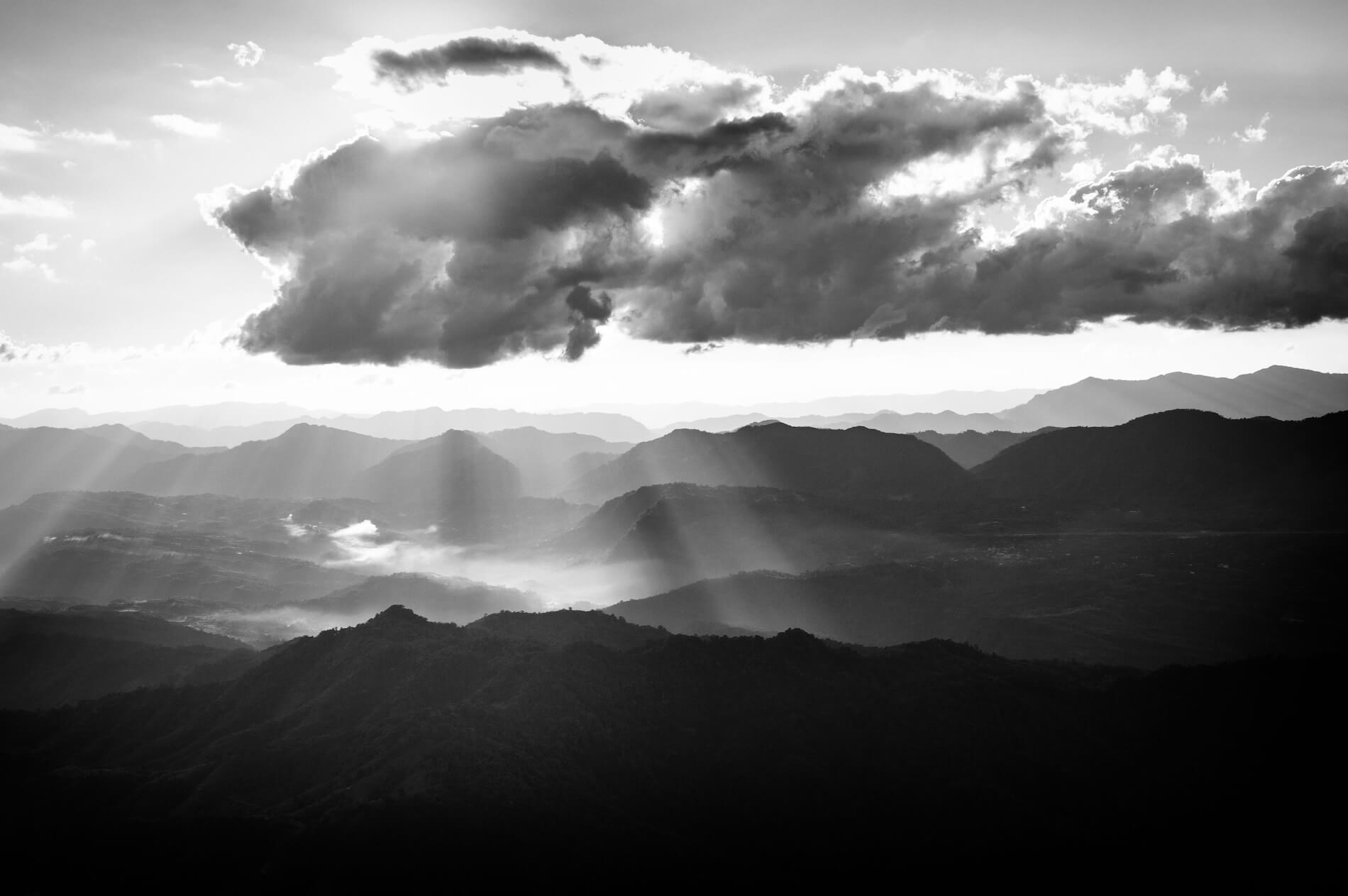 Fine art black and white photograph of a Mizoram landscape in India, with rolling hills beneath drifting clouds