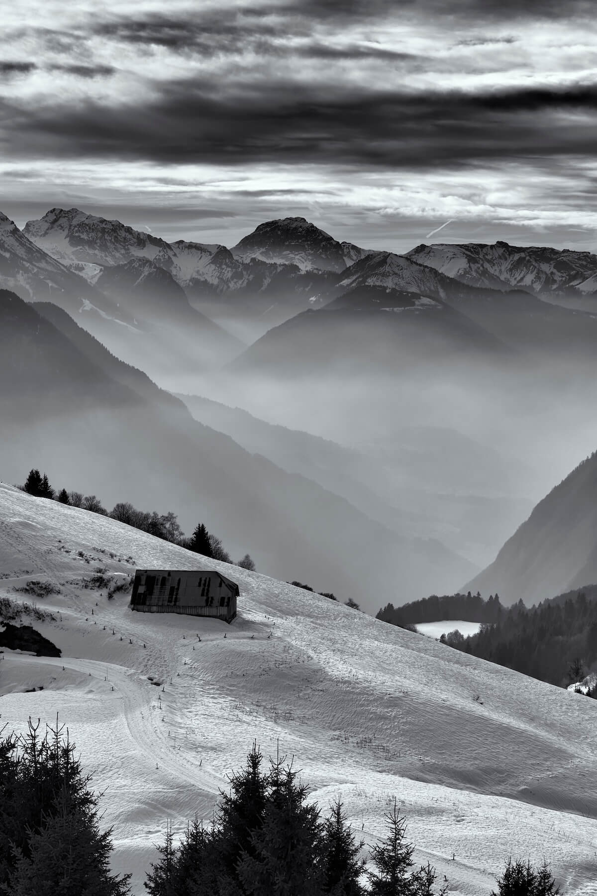 Fine art black and white photograph of a snowy chalet surrounded by a magical mountain landscape