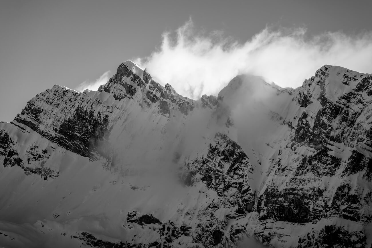 Fine art black and white photograph of snowy mountain peaks surrounded by silky drifting clouds