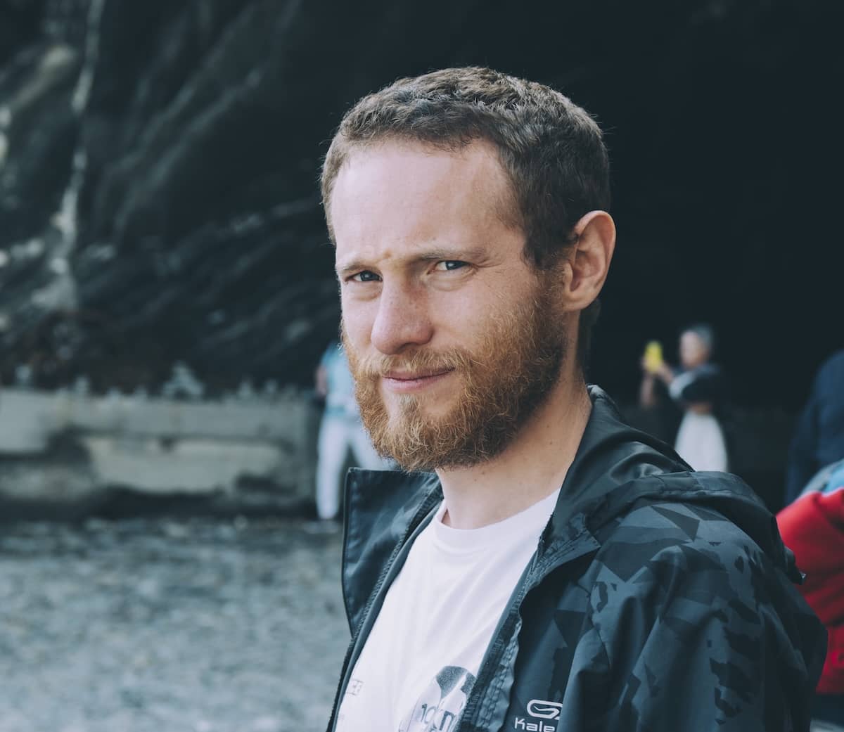 Lose-up cinematic portrait of a bearded man with intense blue eyes wearing a dark patterned jacket against a rocky coastal background in the Cinque Terre in Italy.