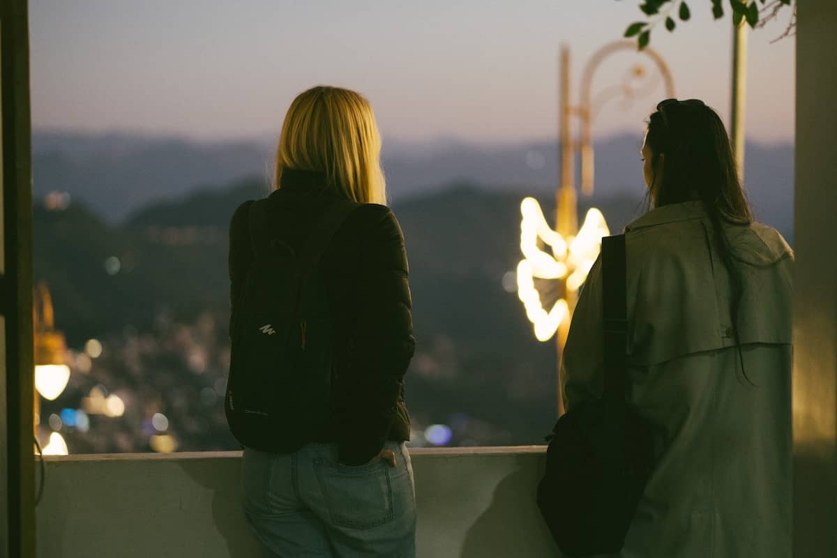 Candid evening shot from behind of two women looking out over a mountainous landscape with distant city lights and glowing decorations in Aizawl, Mizoram.
