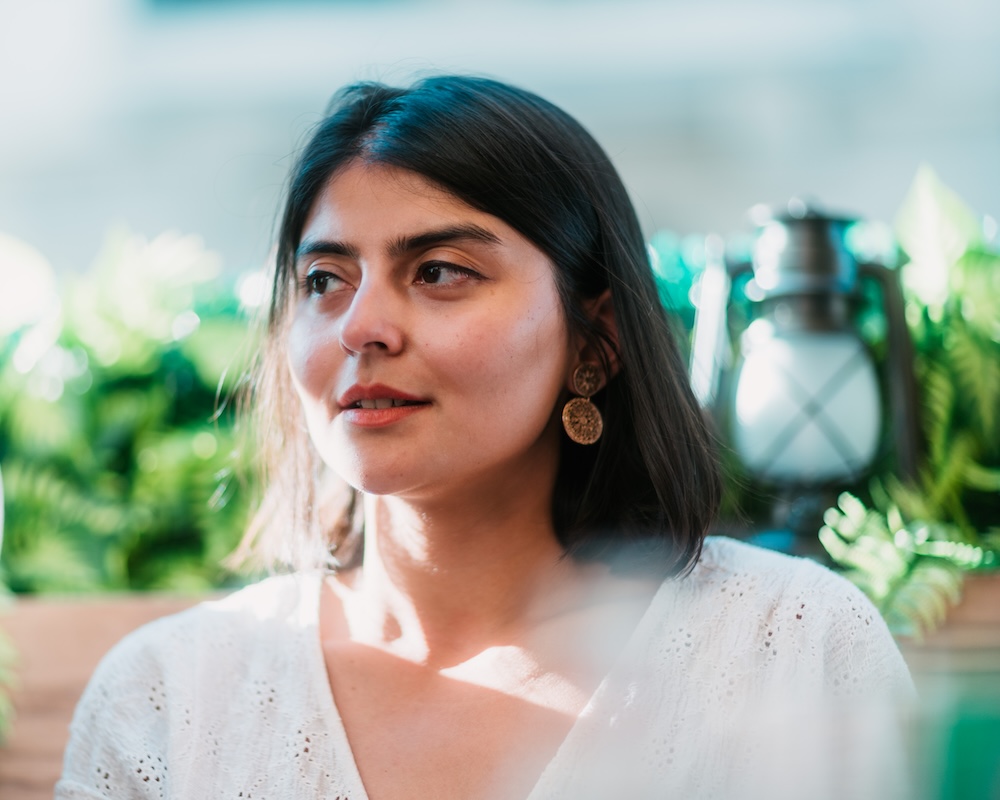 Cinematic candid portrait of a woman looking off-camera in warm light, utilizing a dreamy foreground out-of-focus light wash, a beautifully dissolved background with a vintage lantern, and the organic focus roll-off of an ultra-fast lens.