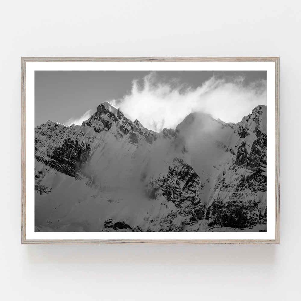 Fine art black and white photograph of snowy mountain peaks surrounded by silky drifting clouds